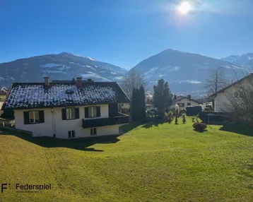 Haus mit Garten und Bergblick unter strahlend blauem Himmel und sonnigem Wetter.