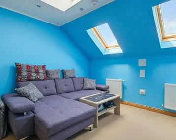 Helles Wohnzimmer im Dachgeschoss mit blauen Wänden, gemütlichem Sofa und mehreren Dachfenstern.