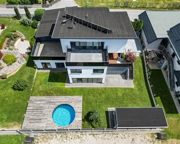 Luftaufnahme eines modernen Hauses mit Garten, Rasenfläche und kleinem runden Pool.