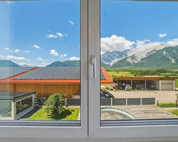 Panoramablick aus dem Fenster auf majestätische Berge, Solaranlagen und den Poolbereich des Anwesens.