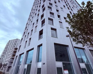 Modernes Hochhaus mit markanter Wellblechfassade und großen Fenstern unter bewölktem Himmel.