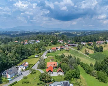 Luftaufnahme einer hügeligen Landschaft mit Wohnhäusern, Straßen und weiten Waldgebieten.