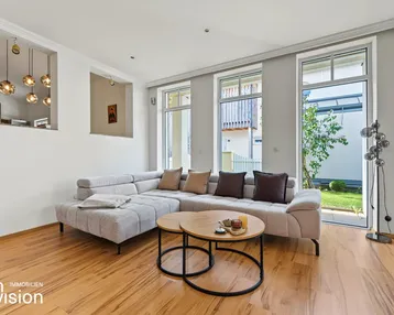 Helles Wohnzimmer mit bequemer Eckcouch, Holzboden und großen Fenstern zum Garten.