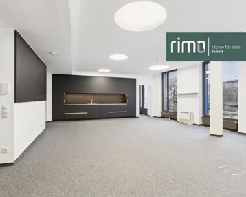Großer, offener Büroraum mit moderner Einbauküche, Teppichboden und großen Fenstern.