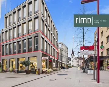Modernes Geschäftsgebäude mit großen Fenstern und Ladenflächen im Erdgeschoss an einer belebten Straße.