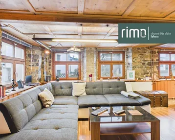 Gemütliches Wohnzimmer mit rustikalen Steinwänden, Holzbalkendecke und großem Ecksofa.