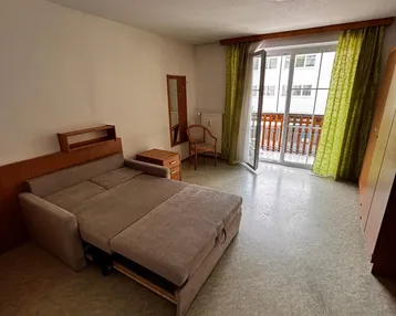 Helles Wohnzimmer mit ausziehbarem Schlafsofa und Zugang zum Balkon, mit Vinylboden.