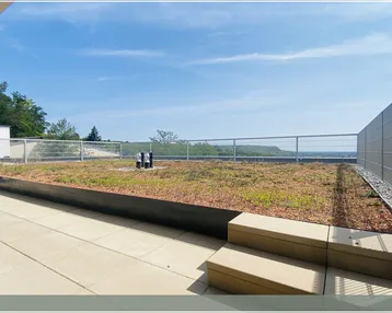 Große Dachterrasse mit Fliesenboden, Gründach und weitem Ausblick in die Landschaft.
