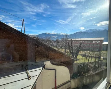 Fensterblick auf die umliegende Landschaft mit Bergen und Gebäuden im Hintergrund.