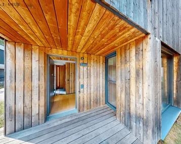 Eingangsbereich des modernen Hauses mit Holzfassade und einer einladenden Holzterrasse.
