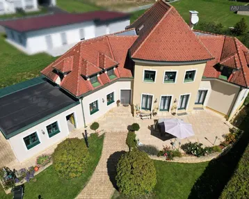 Luftaufnahme eines großen Hauses mit rotem Ziegeldach, weitläufigem Garten und gepflasterter Terrasse.