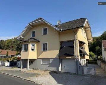 Gelbes Einfamilienhaus mit Satteldach, Garage im Untergeschoss und Balkon.