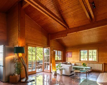 Geräumiges Wohnzimmer im Chalet-Stil mit Holzwänden, hohen Decken und Zugang zur Terrasse.