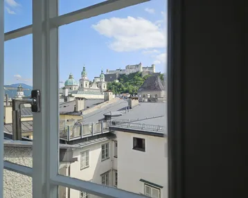 Blick aus dem Fenster auf die historische Stadt Salzburg mit Festung Hohensalzburg und Dächern.