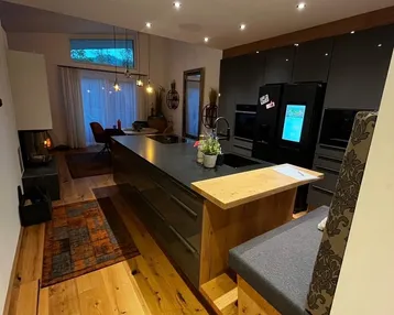 Moderne Küche mit Kochinsel, integrierten Geräten, Holzboden und einem gemütlichen Kamin im Hintergrund.