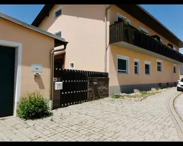 Ansicht des Gebäudes von außen mit gepflasterter Zufahrt und einem Nebengebäude.