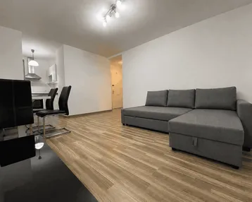 Helles, offenes Wohnzimmer mit Sofa, Esstisch und Blick auf die Küche.