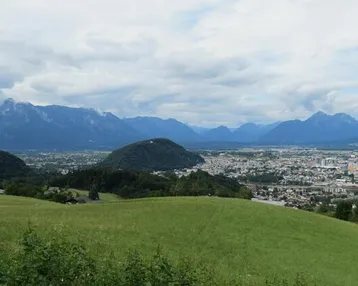 Weitläufiger Blick über eine grüne Landschaft mit einer Stadt im Tal und majestätischen Bergen im Hintergrund.