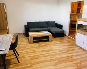 Helles Wohn- und Esszimmer mit Laminatboden, Sofa und einem Blick in die angrenzende Küche.