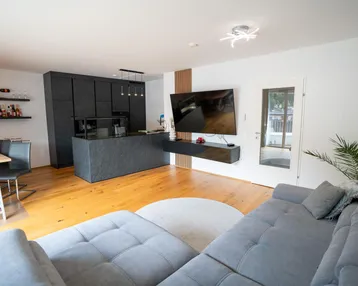Geräumiger Wohnbereich mit bequemer Couch, moderner Küche und Zugang zum Außenbereich.