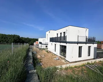 Moderne weiße Neubauhäuser mit Balkonen in einer ländlichen Umgebung unter blauem Himmel.