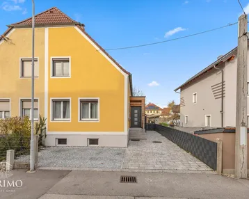 Gelbes Einfamilienhaus mit gepflasterter Einfahrt, Vorgarten und Satteldach.