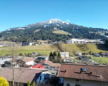 Panoramablick auf schneebedeckte Berge und grüne Täler unter blauem Himmel.