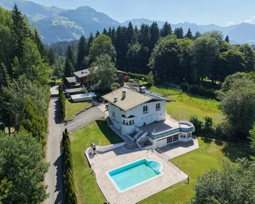 Luftaufnahme des Anwesens mit großem Pool, umgeben von grünen Wiesen und bewaldeten Bergen.