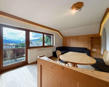 Helles Wohn- und Esszimmer mit Holzelementen, gemütlicher Sitzecke und Zugang zum Balkon mit Bergblick.