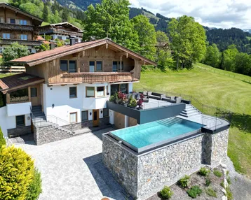 Großzügiges Chalet mit Infinity-Pool, großer Terrasse und Bergblick in grüner Umgebung.