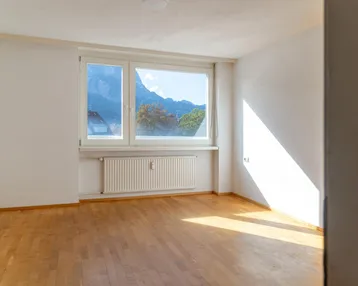 Helles Zimmer mit Parkettboden, weißen Wänden und einem schönen Bergblick durch das Fenster.