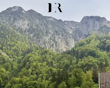 Panoramablick auf bewaldete Berge mit einem Teil eines Daches im Vordergrund.
