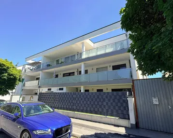 Modernes Mehrfamilienhaus mit mehreren Balkonen und klaren Linien unter blauem Himmel.