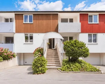 Mehrfamilienhaus mit farbigen Fassadenelementen, Balkonen und Garagen im Reihenhausstil.