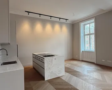Moderne Küche mit Kochinsel, Fischgrätparkett und hohen Fenstern in einem hellen Raum.