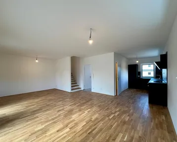 Heller offener Wohnbereich mit Parkettboden und Blick auf die moderne Küche sowie die Treppe.