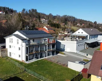 Luftaufnahme des modernen Mehrfamilienhauses mit Solaranlage und umliegender grüner Landschaft.