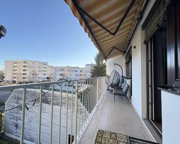 Geräumiger Balkon mit Markise, Sitzgelegenheiten und Blick auf die umliegenden Gebäude.