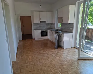 Heller Wohn- und Essbereich mit integrierter Küche, Parkettboden und Zugang zum Balkon.