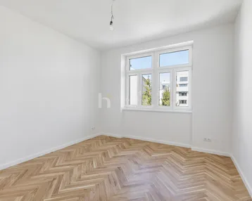 Helles, leeres Zimmer mit Fischgrätparkett und großem Fenster, bereit zum Einzug.