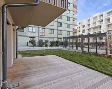 Geräumige Holzterrasse mit angrenzender Rasenfläche und Blick auf moderne Wohngebäude.