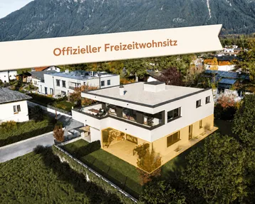 Moderne Villa mit Flachdach und großen Fensterfronten in alpiner Umgebung mit Bergblick.