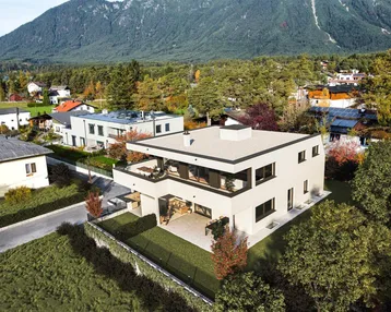 Moderne Architektur eines Neubaus mit Flachdach, umgeben von viel Grün und Bergblick.