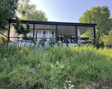 Charmantes Haus mit überdachter Terrasse und üppiger Vegetation in sonniger Lage.