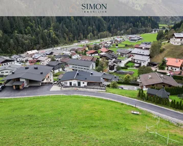 Luftaufnahme eines malerischen Dorfes in einem grünen Tal, umgeben von bewaldeten Bergen und Hügeln.