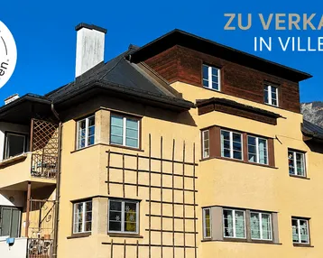 Gelbe Fassade eines Hauses in Villenlage mit Blick auf die Berge und blauen Himmel.