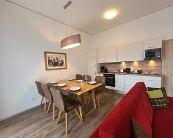 Moderner Essbereich mit Holztisch und integrierter Küche in hellem Design.