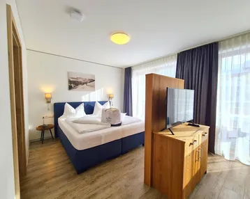 Helles Schlafzimmer mit Doppelbett, Holzboden und Zugang zu einem Balkon mit Bergblick.