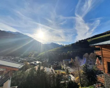 Panoramablick auf die sonnige Berglandschaft mit Tal, Häusern und blauem Himmel.