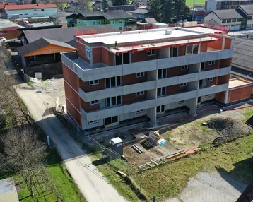 Luftaufnahme eines im Bau befindlichen Mehrfamilienhauses mit Rohbau und umliegender Bebauung.